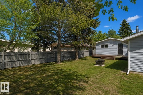 Spacious backyard featuring a mature tree canopy, level lawn, wooden fence perimeter, and detached outbuilding - 4712 49 Street, Calmar, AB - Outdoor
