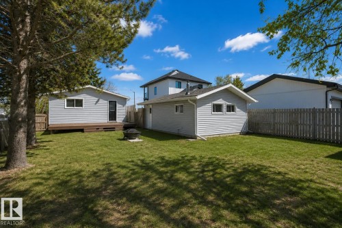 Expansive grassy yard featuring a detached shed with a wood-finish deck, a separate detached garage, and mature trees providing shade - 4712 49 Street, Calmar, AB - Outdoor With Exterior