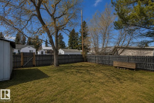 Spacious yard featuring a manicured lawn, full privacy fencing, and a mature shade tree - 4712 49 Street, Calmar, AB - Outdoor