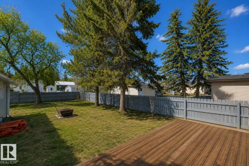 Spacious backyard featuring a wood-finish deck, a fire pit, mature evergreen trees, and perimeter fencing - 4712 49 Street, Calmar, AB - Outdoor