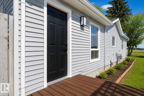 Exterior entry featuring a dark paneled door, light gray horizontal siding, and a wooden deck - 4712 49 Street, Calmar, AB - Outdoor With Exterior
