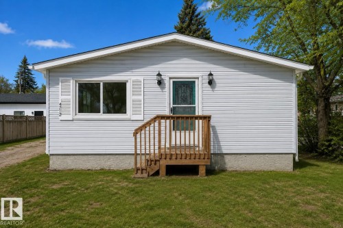 White vinyl siding exterior with a wood-finish porch and railings - 4712 49 Street, Calmar, AB - Outdoor With Exterior