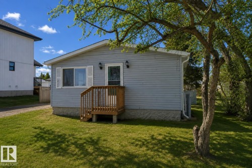 Light gray siding exterior with a wood-tone entry deck, white window trim, and dual exterior wall sconces - 4712 49 Street, Calmar, AB - Outdoor With Exterior
