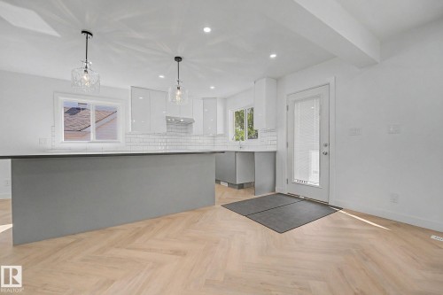Contemporary kitchen featuring a gray island with a dark countertop, light wood-finish flooring in a herringbone pattern, white subway tile backsplash, recessed lighting, and two decorative pendant lights - 10570 66 Avenue Nw, Edmonton, AB - Indoor Photo Showing Kitchen