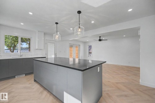 Modern kitchen featuring a spacious island with a dark countertop, two clear glass pendant lights, recessed ceiling lighting, and light wood-finish herringbone flooring - 10570 66 Avenue Nw, Edmonton, AB - Indoor Photo Showing Kitchen
