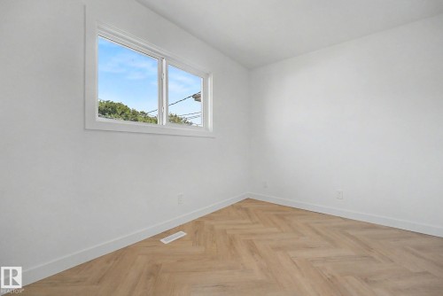 Bright room featuring a horizontal window with white trim, light wood-finish flooring in a herringbone pattern, white baseboards, and neutral wall finishes - 10570 66 Avenue Nw, Edmonton, AB - Indoor Photo Showing Other Room