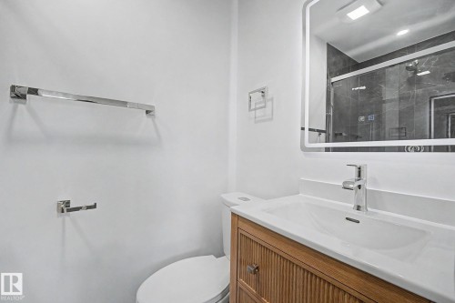Bathroom featuring a wood-finish vanity with a white countertop, an integrated rectangular sink, and a chrome single-handle faucet - 10570 66 Avenue Nw, Edmonton, AB - Indoor Photo Showing Bathroom