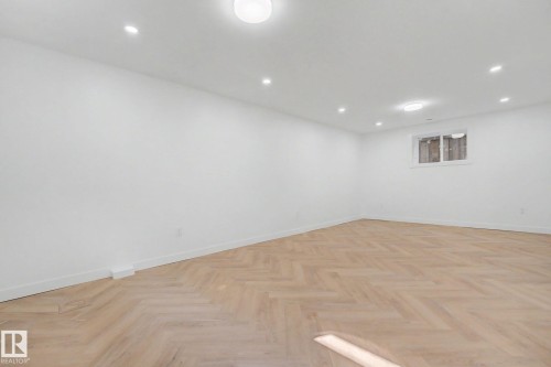 Spacious room featuring herringbone wood-finish flooring, white baseboards, recessed lighting, and a single window with white trim - 10570 66 Avenue Nw, Edmonton, AB - Indoor Photo Showing Other Room