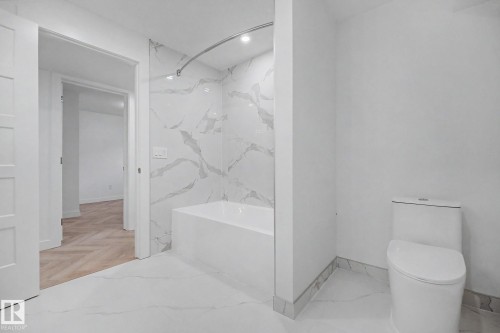 Bathroom featuring a deep soaking tub with surrounding large-format marble-look tile, coordinating floor tile, a white toilet, and a recessed ceiling light - 10570 66 Avenue Nw, Edmonton, AB - Indoor Photo Showing Bathroom