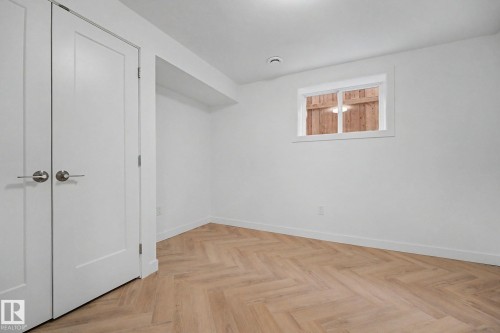 Neutral-toned room featuring a window, light-hued wood-finish flooring in a herringbone pattern, white baseboards, and a pair of white doors with brushed nickel hardware - 10570 66 Avenue Nw, Edmonton, AB - Indoor Photo Showing Other Room