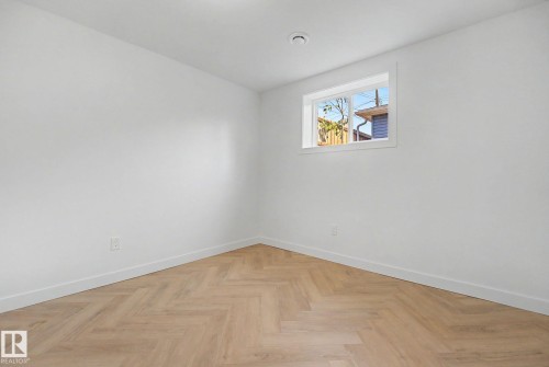 Room featuring wood-finish flooring in a herringbone pattern, crisp white walls, and a window providing natural light - 10570 66 Avenue Nw, Edmonton, AB - Indoor Photo Showing Other Room