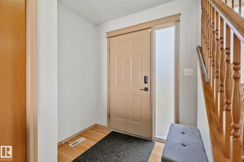 Entryway featuring a panel door with sidelight, wood-finish flooring, and a natural wood staircase - 2819 33 Street Nw, Edmonton, AB - Indoor Photo Showing Other Room