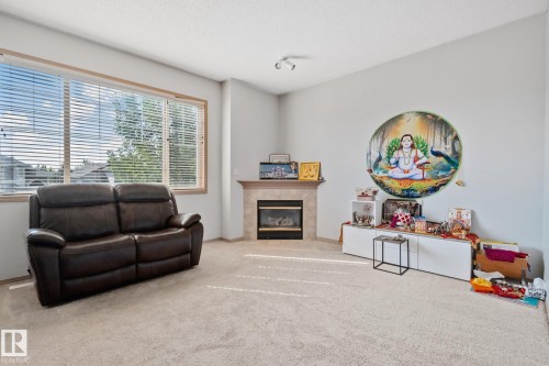 Living area featuring expansive windows, a fireplace with a tile surround and mantel, light-toned carpeting, and track lighting - 2819 33 Street Nw, Edmonton, AB - Indoor Photo Showing Other Room With Fireplace