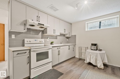 Galley kitchen featuring light gray cabinetry, coordinating subway tile backsplash, white countertops, and wood-finish flooring - 2819 33 Street Nw, Edmonton, AB - Indoor Photo Showing Kitchen