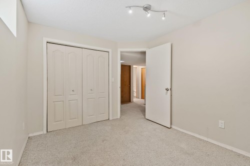 Neutral-toned room featuring a double bifold closet, light-colored carpeting, a white interior door, and track lighting - 2819 33 Street Nw, Edmonton, AB - Indoor