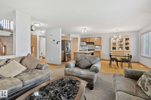 Open-concept living area featuring a kitchen with wood cabinetry and stainless steel appliances, a dining area with wood-finish flooring, and a staircase with wood banisters - 2819 33 Street Nw, Edmonton, AB - Indoor Photo Showing Living Room