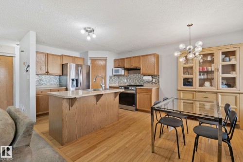 Kitchen featuring wood-finish cabinetry, stainless steel appliances, a center island with sink, and light-toned countertops - 2819 33 Street Nw, Edmonton, AB - Indoor Photo Showing Kitchen