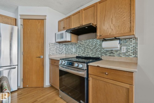 Kitchen featuring wood cabinetry, stainless steel appliances, a mosaic tile backsplash, and light-toned countertops - 2819 33 Street Nw, Edmonton, AB - Indoor Photo Showing Kitchen