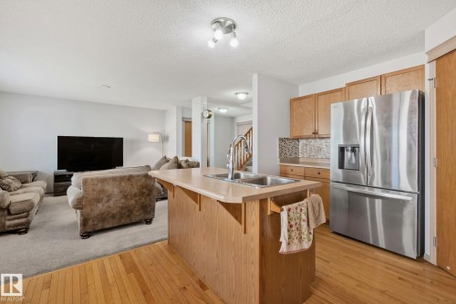 Kitchen island with integrated sink, stainless steel appliances, wood-finish cabinetry, tile backsplash, and wood-finish flooring - 2819 33 Street Nw, Edmonton, AB - Indoor Photo Showing Kitchen With Double Sink