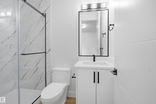 Bathroom featuring a glass-enclosed shower with marble-look wall tiles, a white vanity with a rectangular sink, black-framed mirror, and contemporary matte black fixtures - 304 33 Avenue Nw, Edmonton, AB - Indoor Photo Showing Bathroom