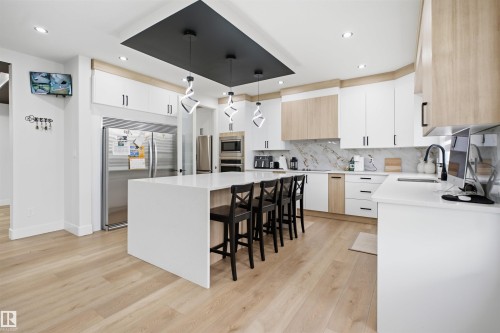 Gourmet kitchen featuring a large central island with seating, white shaker-style cabinetry, stainless steel appliances, and wood-finish flooring - 304 33 Avenue Nw, Edmonton, AB - Indoor Photo Showing Kitchen With Upgraded Kitchen