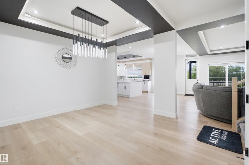 Spacious interior featuring light wood-finish flooring throughout, a modern linear chandelier, recessed lighting, and white baseboards - 304 33 Avenue Nw, Edmonton, AB - Indoor Photo Showing Other Room