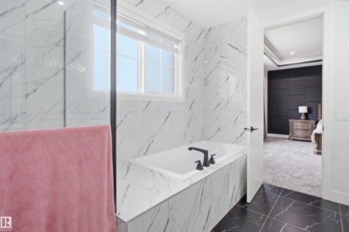 Bathroom featuring a built-in tub with matte black fixtures, marble-patterned wall tiling, a glass-enclosed shower, black marble-patterned floor tiling, and a window for natural light - 304 33 Avenue Nw, Edmonton, AB - Indoor Photo Showing Bathroom