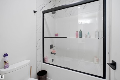Glass-enclosed shower-tub combination featuring matte black hardware and a white marble-look tiled surround - 304 33 Avenue Nw, Edmonton, AB - Indoor Photo Showing Bathroom