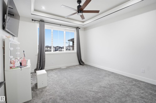 Spacious room featuring a large window, tray ceiling with recessed lighting, ceiling fan with wood-finish blades, and neutral gray carpeting - 304 33 Avenue Nw, Edmonton, AB - Indoor Photo Showing Other Room
