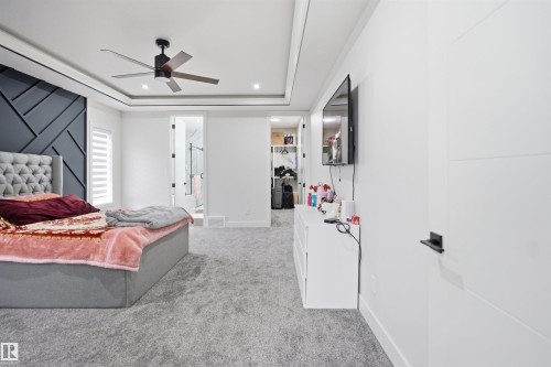 Spacious room featuring tray ceilings, a modern ceiling fan, and a striking accent wall with geometric paneling - 304 33 Avenue Nw, Edmonton, AB - Indoor Photo Showing Bedroom
