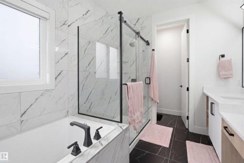 Bathroom featuring a built-in tub with matte black fixtures, a walk-in shower with a glass enclosure and black frame, black marble-look floor tile, and white marble-look wall tile - 304 33 Avenue Nw, Edmonton, AB - Indoor Photo Showing Bathroom