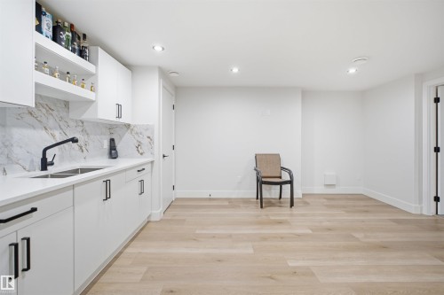 Modern wet bar featuring white cabinetry with matte black hardware, dual stainless steel sink, and quartz countertops with a full-height stone-look backsplash - 304 33 Avenue Nw, Edmonton, AB - Indoor Photo Showing Other Room