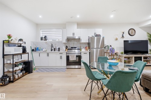 Contemporary kitchen featuring white cabinetry, stainless steel appliances, a marble-patterned backsplash, and light wood-finish flooring - 304 33 Avenue Nw, Edmonton, AB - Indoor