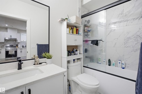 Bathroom with a white vanity featuring a matte black faucet, a large frameless mirror, and a full-sized bathtub with a sliding glass door - 304 33 Avenue Nw, Edmonton, AB - Indoor Photo Showing Bathroom