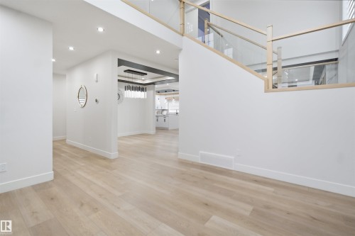 Expansive interior featuring light wood-finish flooring throughout, a modern glass and wood-frame staircase, recessed lighting, and a contemporary chandelier - 304 33 Avenue Nw, Edmonton, AB - Indoor Photo Showing Other Room