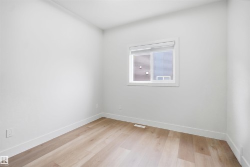 Bright interior space featuring a window with a roller shade, light wood-finish flooring, white baseboards, and neutral wall tones - 304 33 Avenue Nw, Edmonton, AB - Indoor Photo Showing Other Room