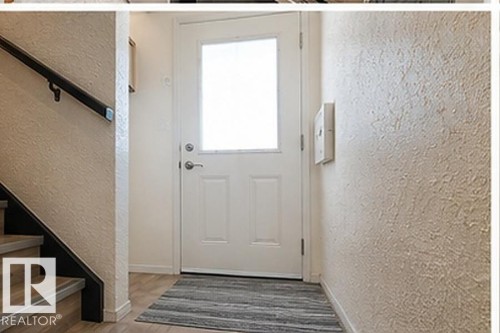 Entryway featuring a white paneled door with frosted glass, wood-finish flooring, and a staircase with a dark handrail and light wood-finish treads - 7812 144 Avenue Nw, Edmonton, AB - Indoor Photo Showing Other Room