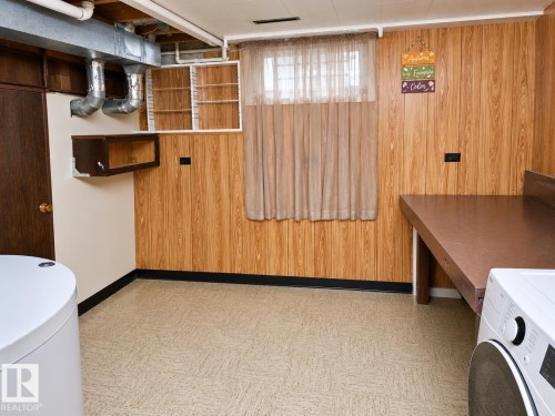 Utility space featuring wood-finish wall paneling, a large window with sheer curtain, exposed overhead ductwork and piping, and durable flooring - 7812 144 Avenue Nw, Edmonton, AB - Indoor Photo Showing Laundry Room
