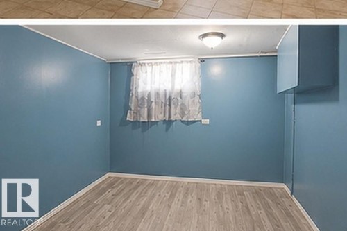 Room featuring blue painted walls, wood-finish flooring, a window with sheer curtains, a flush-mount ceiling light fixture, and a built-in wall cabinet - 7812 144 Avenue Nw, Edmonton, AB - Indoor Photo Showing Other Room