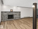 Living area featuring a brick fireplace with a black metal screen, wood-finish flooring, and recessed ceiling lighting - 7812 144 Avenue Nw, Edmonton, AB  - Indoor With Fireplace 
