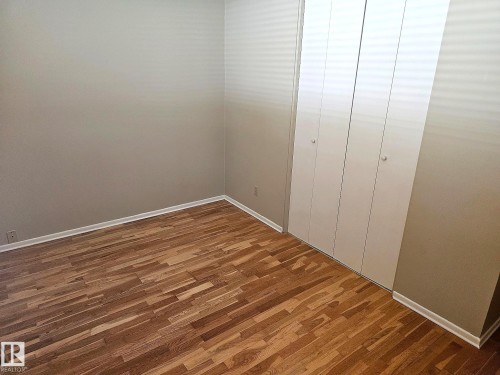 Room featuring wood-finish flooring, light neutral wall paint, white baseboards, and a white bi-fold closet - 7812 144 Avenue Nw, Edmonton, AB - Indoor Photo Showing Other Room