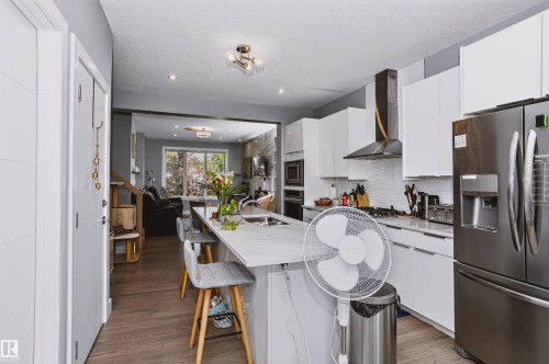 Contemporary kitchen featuring white cabinetry, stainless steel appliances, a white tile backsplash, and wood-finish flooring - 11305 79 Avenue Nw, Edmonton, AB - Indoor Photo Showing Kitchen With Double Sink With Upgraded Kitchen