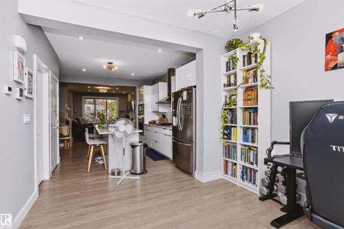 Open-concept main level featuring light wood-finish flooring, recessed lighting, a contemporary chandelier, a built-in bookshelf, and a modern kitchen with stainless steel appliances - 11305 79 Avenue Nw, Edmonton, AB - Indoor