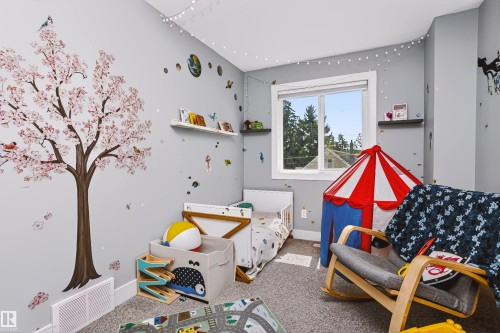 Bright and versatile bedroom featuring soft gray walls, carpeted flooring, and abundant natural light from a large window with forest views - 11305 79 Avenue Nw, Edmonton, AB - Indoor
