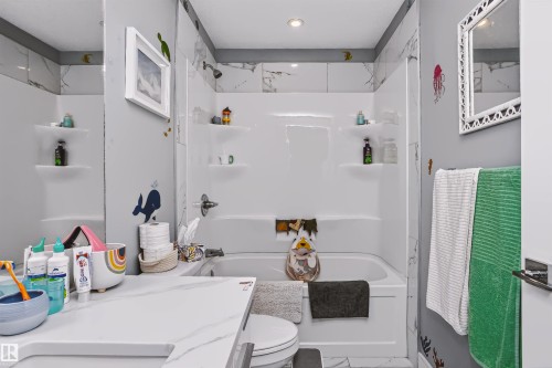 Contemporary bathroom featuring a white tub/shower combination with integrated shelving, chrome fixtures, and a white tiled surround - 11305 79 Avenue Nw, Edmonton, AB - Indoor Photo Showing Bathroom