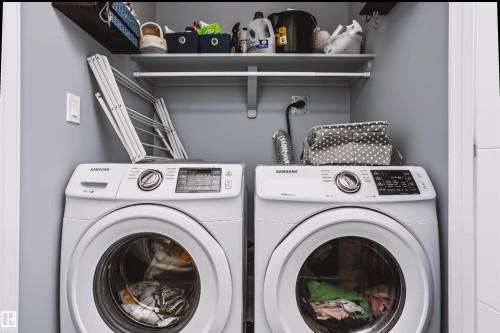 Dedicated laundry area featuring front-loading appliances, white shelving, and a dark wood-finish shelf - 11305 79 Avenue Nw, Edmonton, AB - Indoor Photo Showing Laundry Room