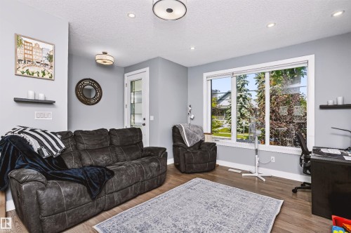 Comfortable family room showcasing a plush reclining sofa, rich wood-finish flooring, and abundant natural light from expansive glass sliding doors - 11305 79 Avenue Nw, Edmonton, AB - Indoor Photo Showing Living Room