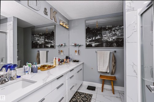 Spacious bathroom featuring a double vanity with integrated sinks, a wide mirror extending across the wall, a shower enclosure with a glass door, and large format white tile flooring with veining - 11305 79 Avenue Nw, Edmonton, AB - Indoor Photo Showing Bathroom