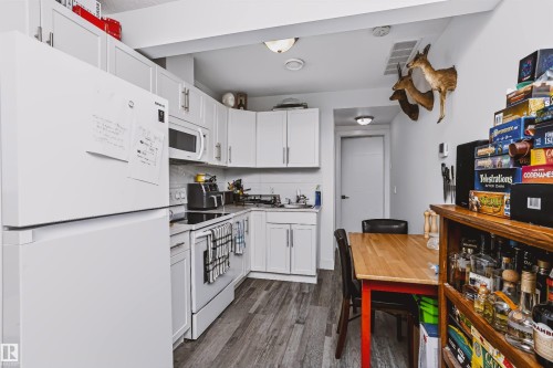 Kitchen featuring white cabinetry, white appliances, wood-finish flooring, and a built-in overhead microwave - 11305 79 Avenue Nw, Edmonton, AB - Indoor Photo Showing Kitchen