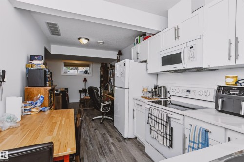 Kitchen featuring white cabinetry with brushed nickel hardware, white appliances including an electric range and built-in microwave, light-toned countertops, and wood-finish flooring - 11305 79 Avenue Nw, Edmonton, AB - Indoor Photo Showing Kitchen